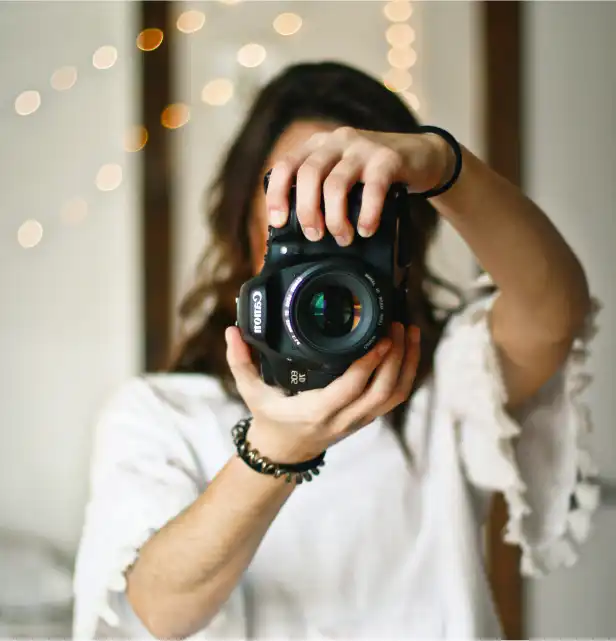 Person holding up a Canon camera, pointing it toward the viewer
