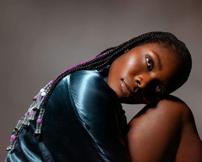 Studio portrait of a woman with braided hair and a metallic jacket, lit dramatically from the side