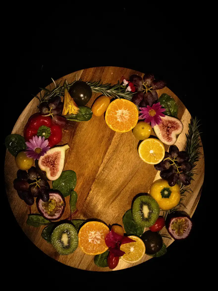 Overhead flat-lay of sliced fruit, flowers and herbs arranged on a wooden board